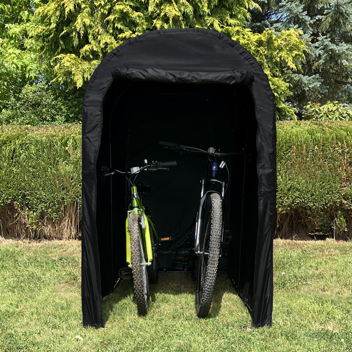 Schwarzes Fahrradzelt mit zwei Fahrrädern, das Schutz bietet, umgeben von grünem Gras und Bäumen im Hintergrund