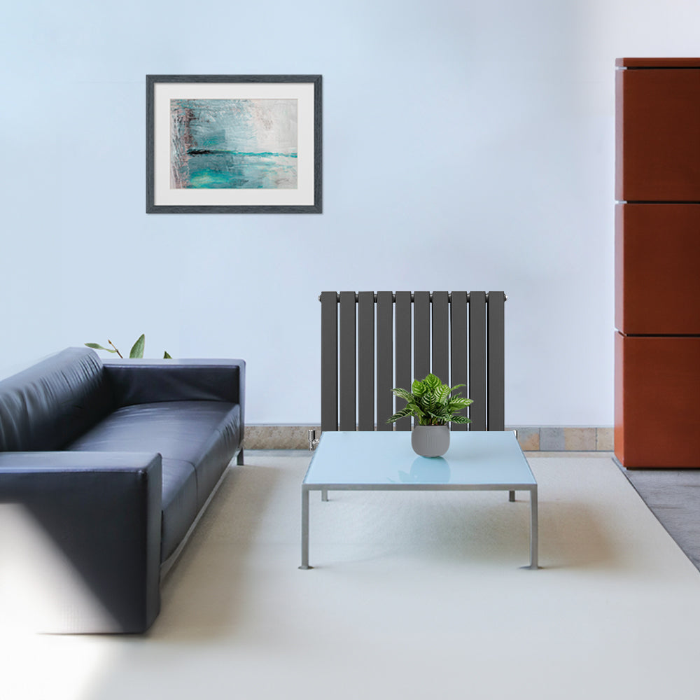 Anthrazitgrauer Paneelheizkörper mit vertikalen Lamellen, 600mm x 700mm, elegant in modernem Wohnzimmer mit Glas-Couchtisch und Pflanzen dekoriert