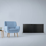 Paneelheizkörper in mattem Schwarz, 600mm x 1400mm, mit schlankem Design und vertikalen Lamellen, elegant neben einem blauen Sessel platziert