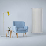 Paneelheizkörper in glänzendem Weiß, 1600mm x 700mm, mit vertikalen Lamellen, neben einem blauen Sessel und einer modernen Stehlampe in gelb