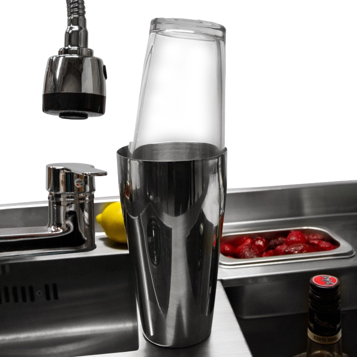 Elegante Cocktail-Bar Station mit glänzendem Edelstahl, transparentem Shaker und frischen Zutaten wie Zitronen und Erdbeeren im Hintergrund