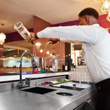 Elegante Cocktail-Bar Station aus Edelstahl mit einem Barkeeper, der einen Drink in einen Shaker gießt, umgeben von frischen Zutaten und Gläsern