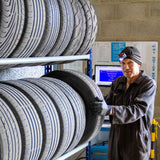 Zwei T-Rax Autoreifenregale mit mehreren Reifen, stabiler Metallrahmen, dunkle Reifen mit Profil, Werkstattumgebung, Person in Arbeitskleidung und Handschuhen