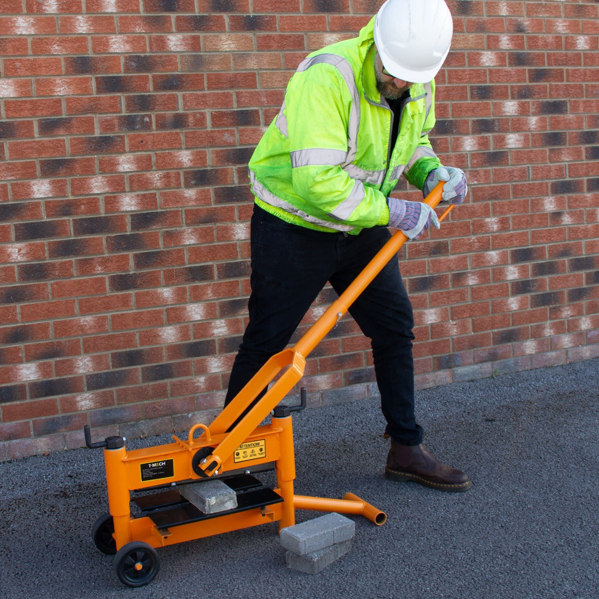 Der T-Mech 330mm Steinknacker in leuchtendem Orange wird von einem Arbeiter in Sicherheitskleidung verwendet, um einen grauen Stein zu trennen