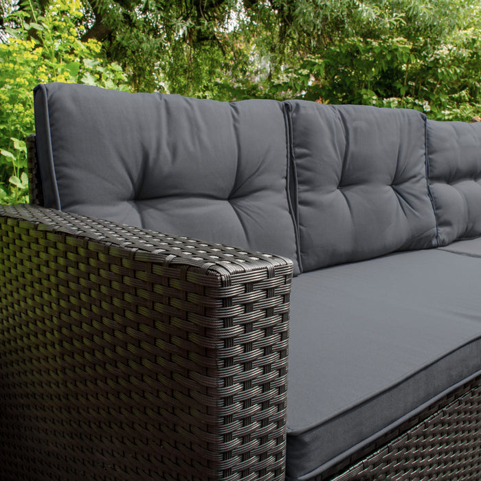 Bequeme, dunkelgraue Polster auf einem eleganten, geflochtenen Rattan-Sofa, ideal für entspannte Stunden im Freien, umgeben von grüner Natur