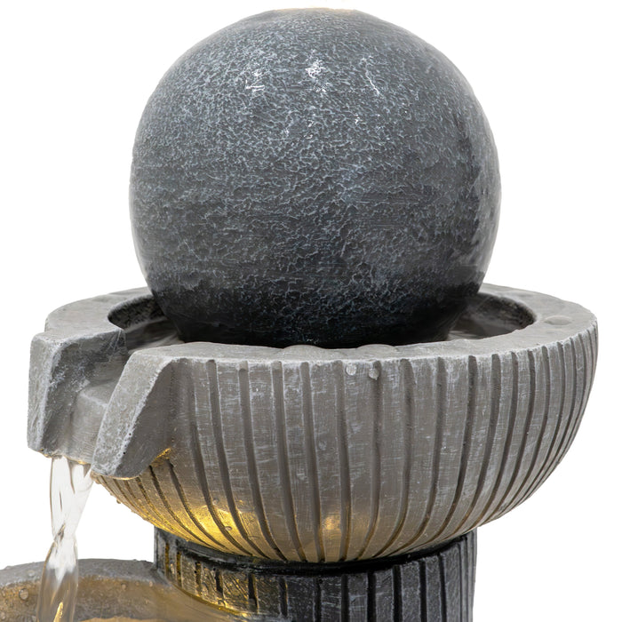 Schwarze Kugelbrunnen mit strukturierter Oberfläche, Wasser fließt sanft über die Kanten in die darunterliegende Schale aus grauem Stein