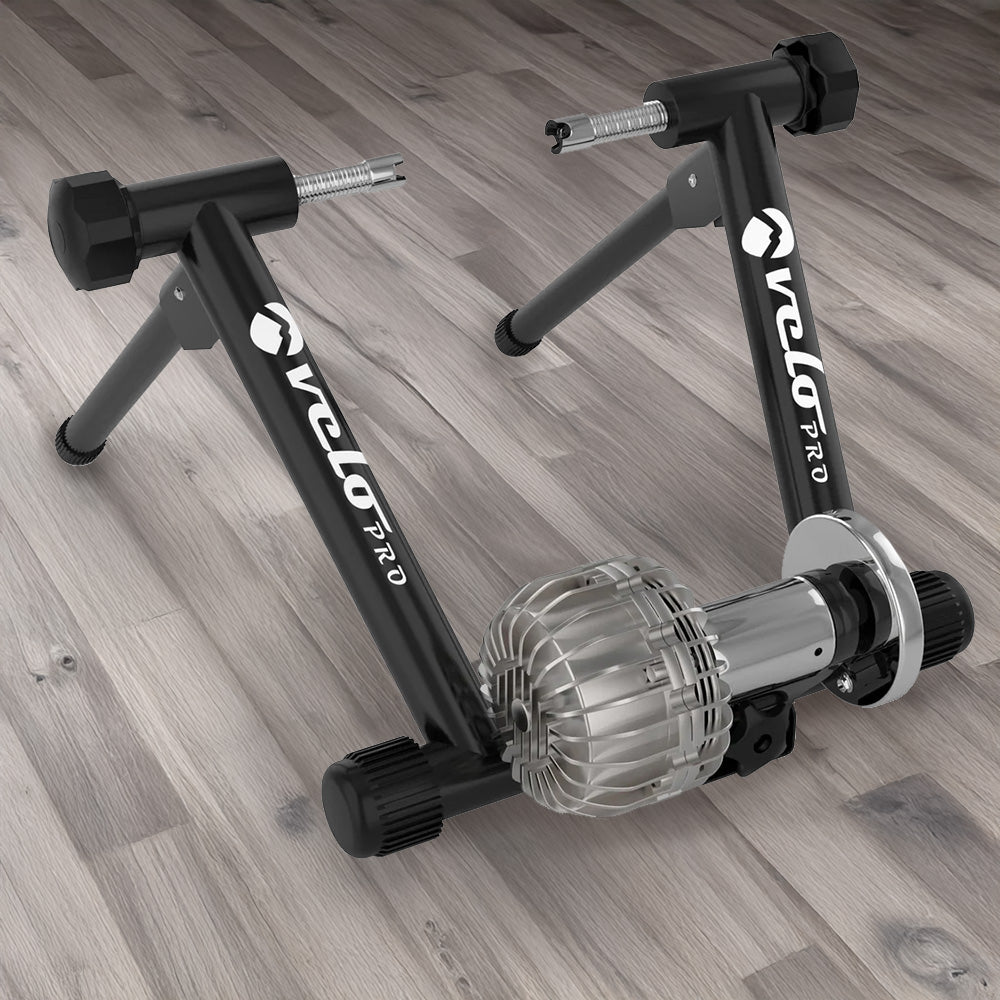 Schwarzer Flüssigkeits-Rollentrainer Velo Pro mit stabilen Füßen und glänzendem, silbernem Antrieb, ideal für das Indoor-Training auf Holzfußboden