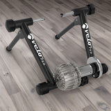 Schwarzer Flüssigkeits-Rollentrainer Velo Pro mit stabilen Füßen und glänzendem, silbernem Antrieb, ideal für das Indoor-Training auf Holzfußboden