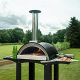Freistehender Outdoor-Pizzaofen mit glänzendem Edelstahl-Schornstein, schwarzem Gehäuse und Vorbereitungsstationen für frische Zutaten im Garten