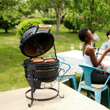 Kamado-Ofen Holzkohlegrill in Schwarz mit rauchenden Würstchen, stilvolles Design, runde Form, auf einem Holztisch im Freien, umgeben von grüner Natur