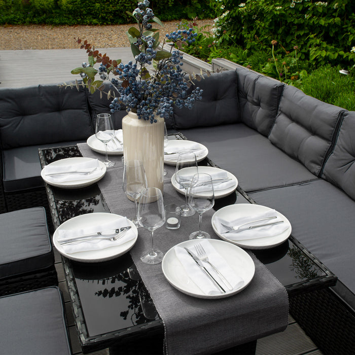 Elegant gedeckter Tisch im Freien mit weißen Tellern, Gläsern und einer stilvollen Vase mit blauen Blumen auf einem modernen, dunklen Tisch