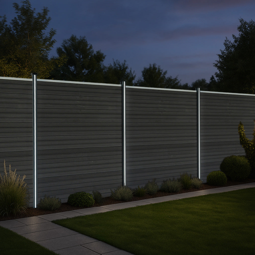 Grau WPC Sichtschutzzaun mit LED Zaunpfosten, moderne, glatte Oberfläche, nachts beleuchtet, umgeben von grünen Pflanzen und einem gepflasterten Weg