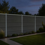 Grau WPC Sichtschutzzaun mit LED Zaunpfosten in der Dämmerung, umgeben von grünen Pflanzen und einem gepflasterten Weg, moderne und elegante Gestaltung