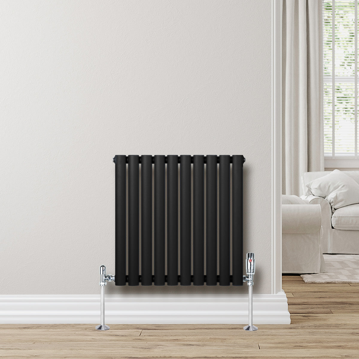 Schwarzer Gliederheizkörper mit TRV Chromventilen, 600mm x 600mm, an einer hellen Wand, umgeben von einem modernen Wohnraum mit Holzfußboden