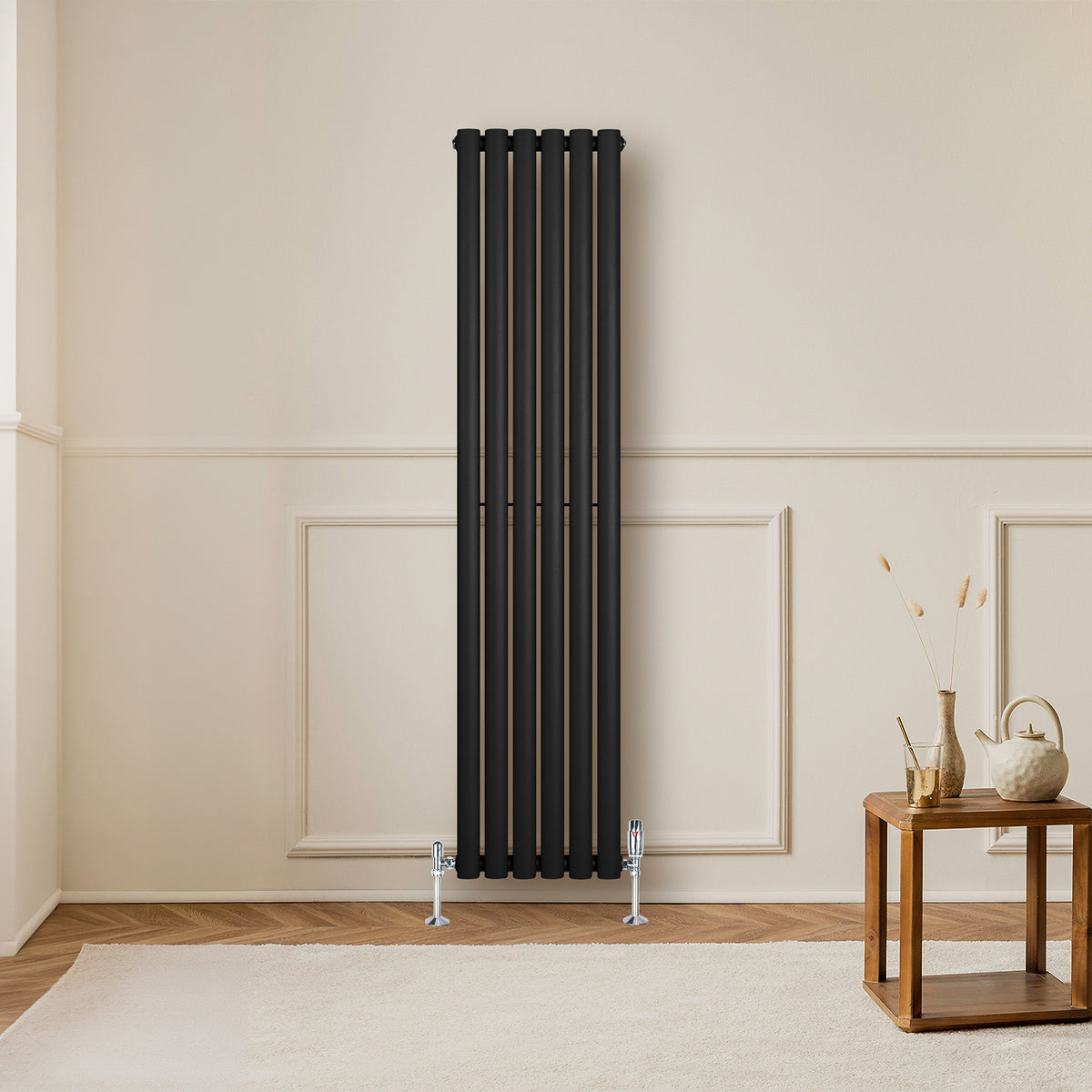 Schwarzer Gliederheizkörper mit TRV Chromventilen, 1600mm x 360mm, an einer hellen Wand, neben einem Holztisch und dekorativen Elementen