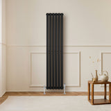 Schwarzer Gliederheizkörper mit TRV Chromventilen, 1600mm x 360mm, an einer hellen Wand, neben einem Holztisch und dekorativen Elementen