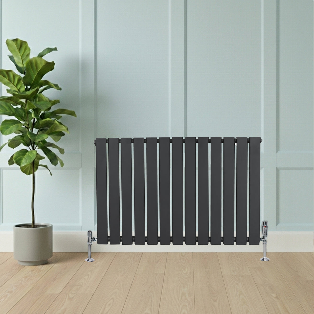 Flachheizkörper in Anthrazitgrau, 600mm x 910mm, mit vertikalen Lamellen und glänzenden Ventilen, vor einer hellen Wand und einem grünen Pflanzenarrangement