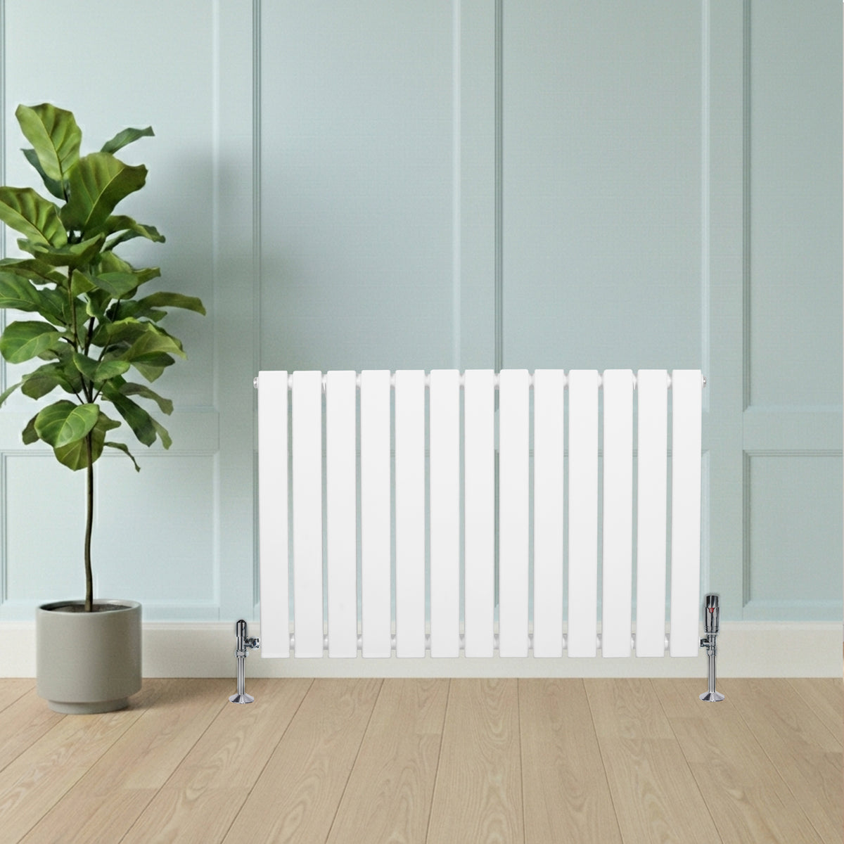 Flachheizkörper in Weiß, 600mm x 910mm, mit vertikalen Lamellen und glänzenden Ventilen, vor einer hellblauen Wand und einer grünen Pflanze platziert