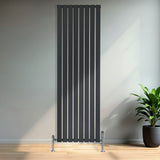 Schmaler schwarzer Flachheizkörper mit vertikalen Lamellen, montiert an einer hellen Wand, vor einem modernen Raum mit Pflanzen im Hintergrund