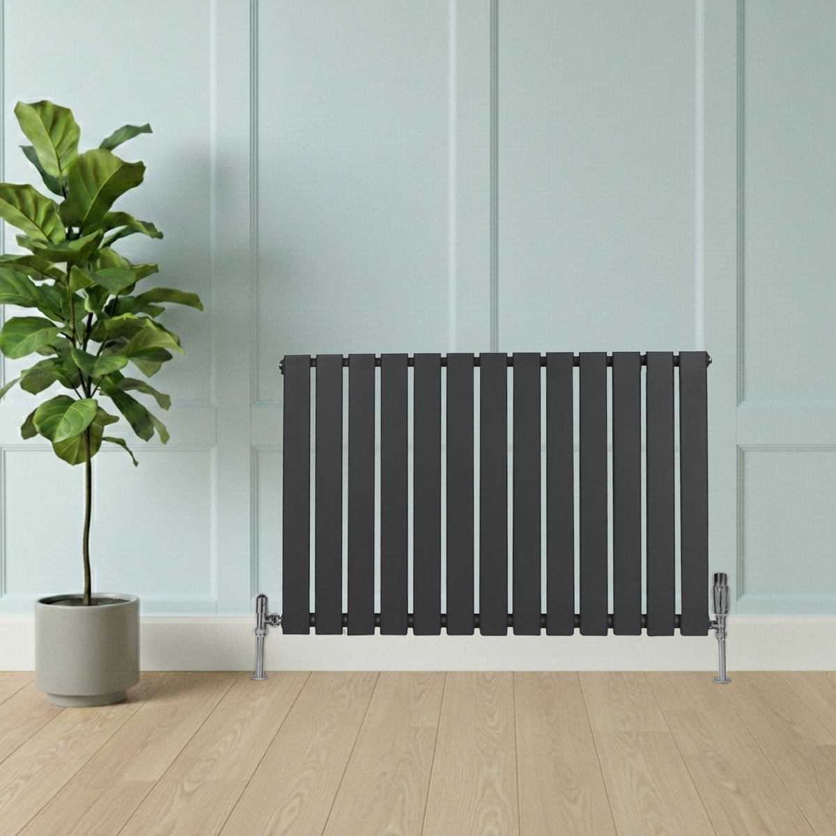 Flachheizkörper in Anthrazitgrau, 600mm x 910mm, mit modernen vertikalen Lamellen und eleganten Ventilen, vor einer hellen Wand und einem Topf mit Pflanze