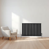 Flachheizkörper in Schwarz, 600mm x 910mm, mit vertikalen Lamellen und glänzenden Metallfüßen, platziert in einem modernen Raum mit Holzfußboden