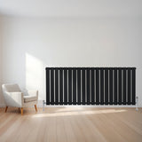 Schwarzer Flachheizkörper mit vertikalen Lamellen, 600mm x 1400mm, elegant an einer hellen Wand, neben einem modernen weißen Sessel auf Holzfußboden