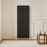 Schwarzer Gliederheizkörper mit vertikalen Lamellen, 1600mm x 600mm, elegant an einer hellen Wand, ergänzt durch einen modernen Holztisch und Dekoration
