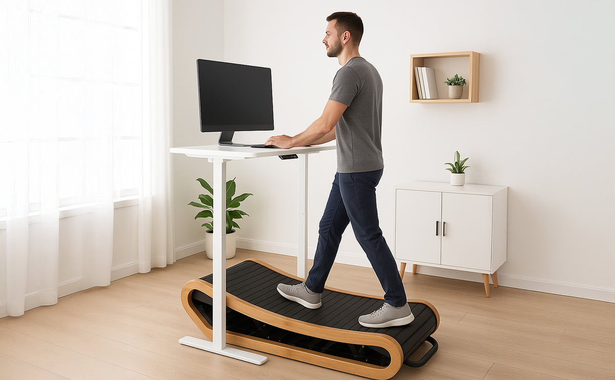 Ein Mann in einem grauen T-Shirt steht auf einem eleganten Laufband mit Holzrahmen, während er an einem modernen Schreibtisch mit Monitor arbeitet