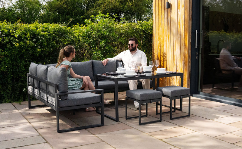 Elegantes Gartenset mit grauen Polstern, moderner Tisch und Stühlen, umgeben von grüner Vegetation, ideal für entspannte Zusammenkünfte im Freien