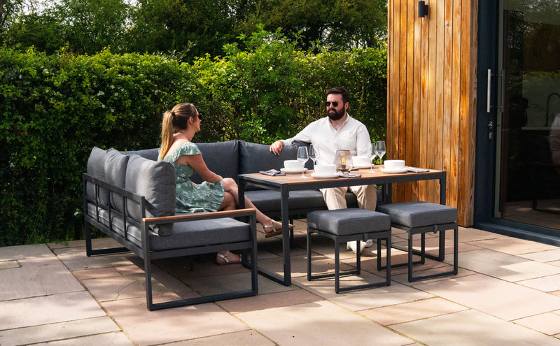 Moderne Gartenmöbel aus grauem Stoff und schwarzem Metall, mit einem Paar, das entspannt an einem Tisch mit Getränken sitzt, umgeben von grüner Natur