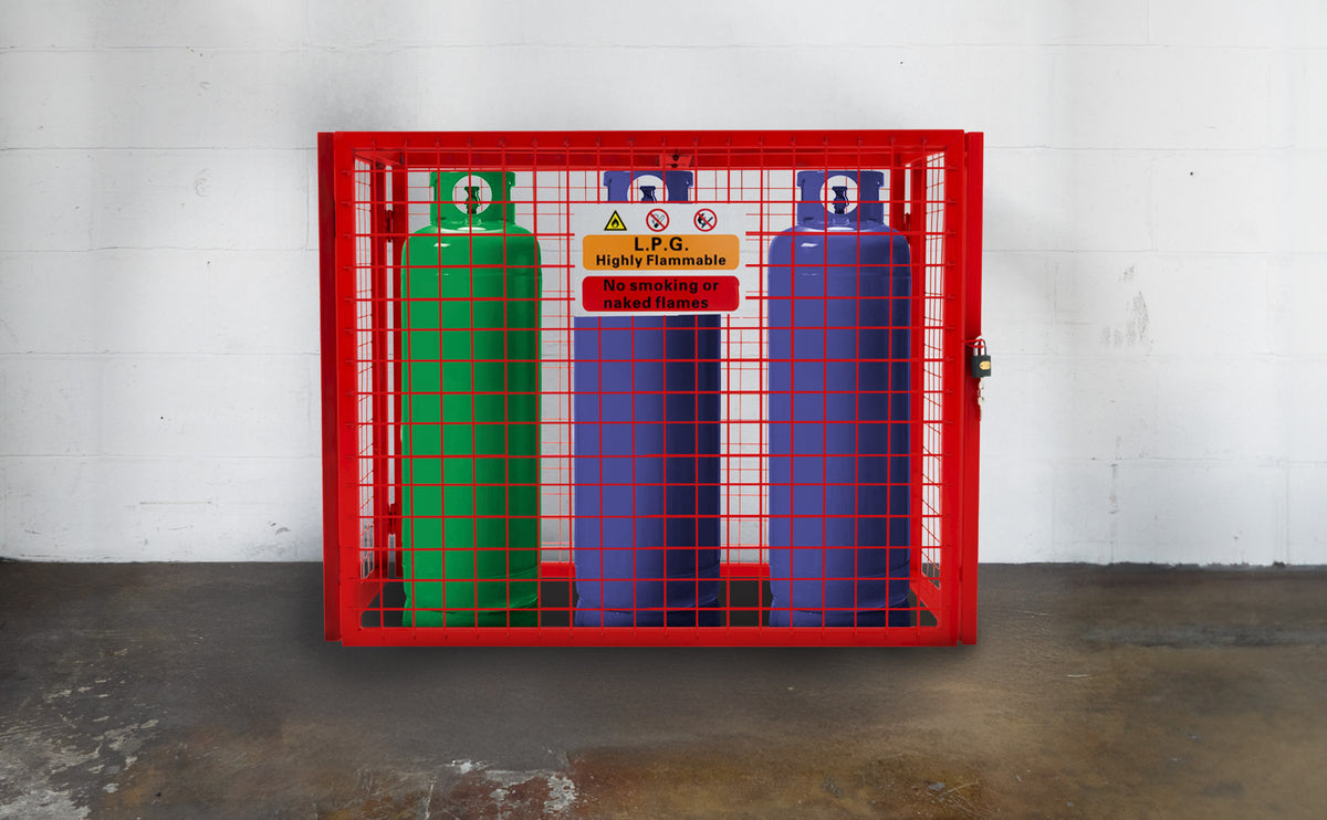 Drei Gasflaschen in einem roten Gitterkäfig, eine grüne, eine lila und eine blaue, mit Warnschild für entzündliche Stoffe und Sicherheitsanweisungen