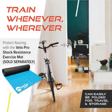 Schwarzer Flüssigkeits-Rollentrainer Velo Pro in einem modernen Raum, neben einem Fahrrad, auf einem hellen Holzboden, mit einer blauen Trainingsmatte im Vordergrund
