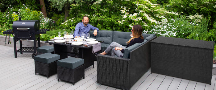 Gemütliche Gartensitzgruppe aus schwarzem Rattan mit grauen Kissen, umgeben von grünen Pflanzen, ideal für gesellige Grillabende im Freien