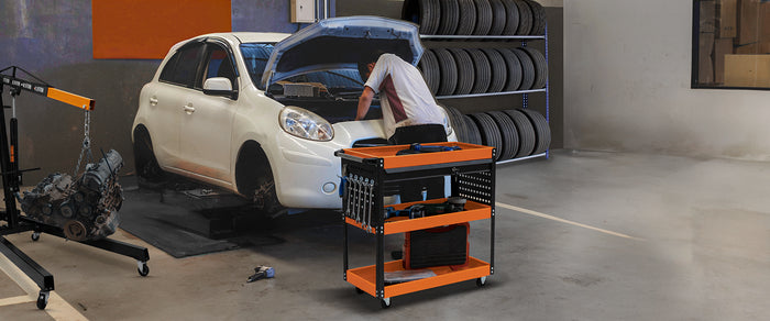 Ein Mechaniker arbeitet an einem weißen Auto mit offenem Motorhaube, während er ein orangefarbenes Werkzeugwagen mit verschiedenen Werkzeugen benutzt