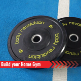 Schwarze Gummi-Bumper mit gelbem Schriftzug "Body Revolution", 15 kg, auf blauer Unterlage, ideal für das Heimtraining und Kraftsport