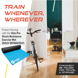 Silberner magnetischer Rollentrainer Velo Pro mit blauer Matte, ideal für das Training zu Hause, auf einem hellen Holzboden in einem modernen Raum