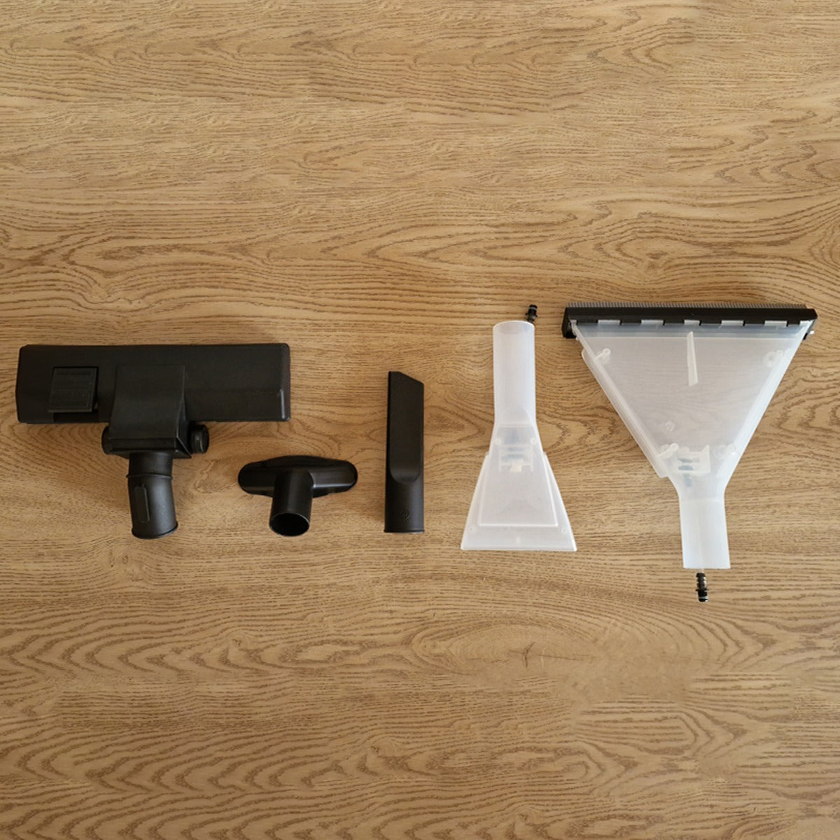 Schwarze und transparente Aufsätze für den MAXBLAST 3 in 1 Shampoo Nass- und Trockensauger, auf einer Holzoberfläche angeordnet, zeigen verschiedene Formen und Funktionen