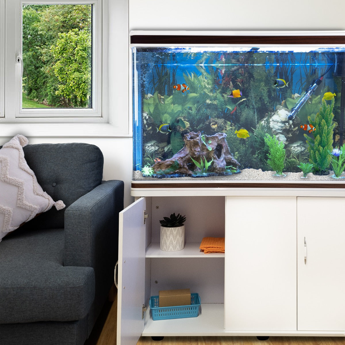 Aquarium Komplettset in Weiß mit bunten Fischen, lebendigen Pflanzen und natürlichem Dekor, platziert neben einem Sofa und Fenster mit Blick ins Freie