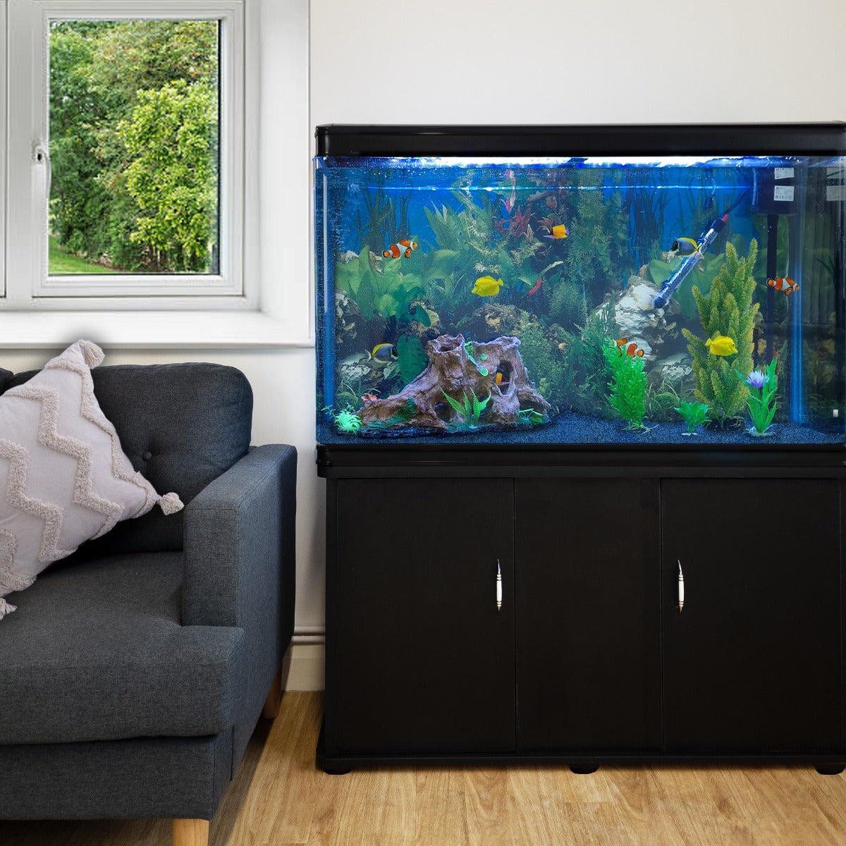 Schwarzes 300L Aquarium-Set mit bunten Fischen, lebendigen Pflanzen und Kies, platziert neben einem grauen Sofa in einem hellen Raum
