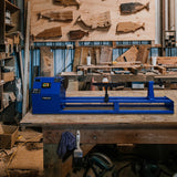 Blau lackierte T-Mech Drechselbank auf einer Holzwerkbank, umgeben von Holzstücken und Werkzeugen in einer Werkstatt, ideal für Holzverarbeitung