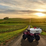 Roter ATV mit 60L Sprühgerät auf einer ländlichen Straße, umgeben von Weinbergen und sanften Hügeln, bei Sonnenuntergang