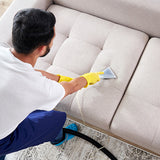 Ein Mann mit gelben Handschuhen reinigt ein hellbeiges Sofa mit einem MAXBLAST 3 in 1 Shampoo Nass- und Trockensauger, während ein schwarzer Schlauch sichtbar ist